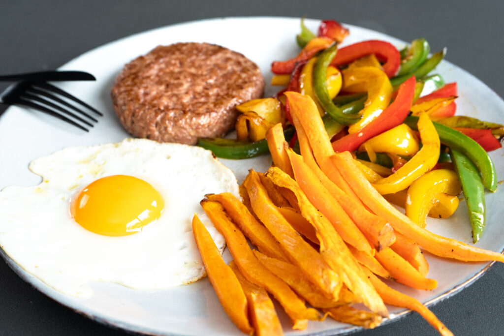 Hamburguesa de heura con pimientos rehogados, huevo a la plancha y boniato asado